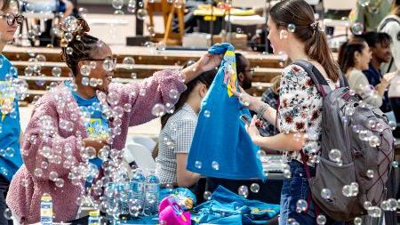 Bubbles floating in the air as a student is handed an Arts Everywhere T-shirt.