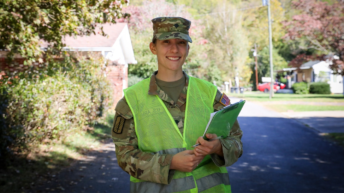 Jessica Bowling posing for a portrait in her National Guard uniform while holding a clipboard while walking around a neighborhood in Waynesville, N.C.