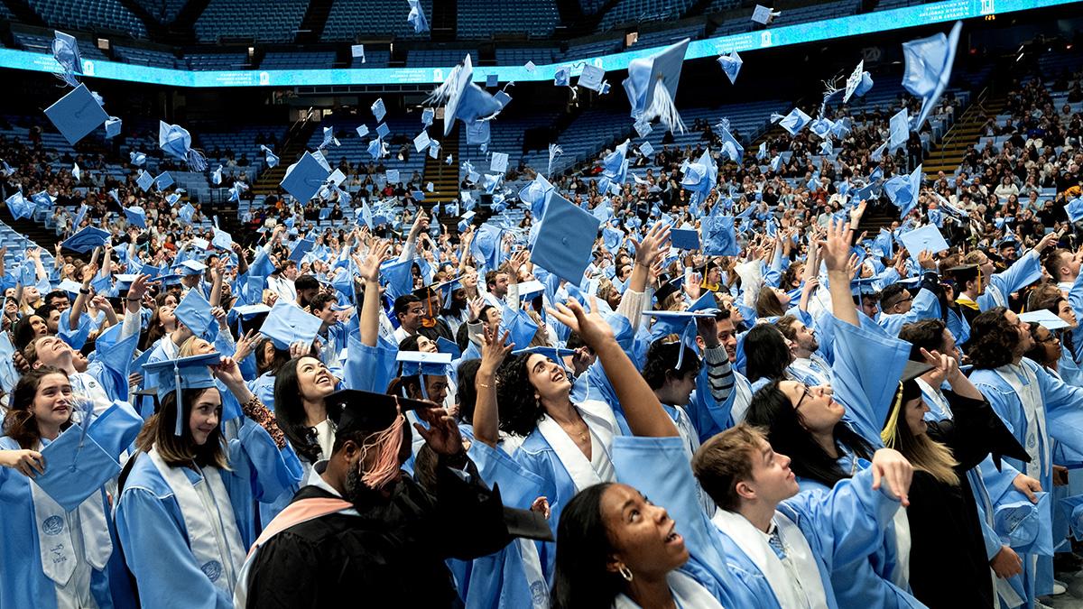 A large crowd of students throwing their graduation caps up in celebration.