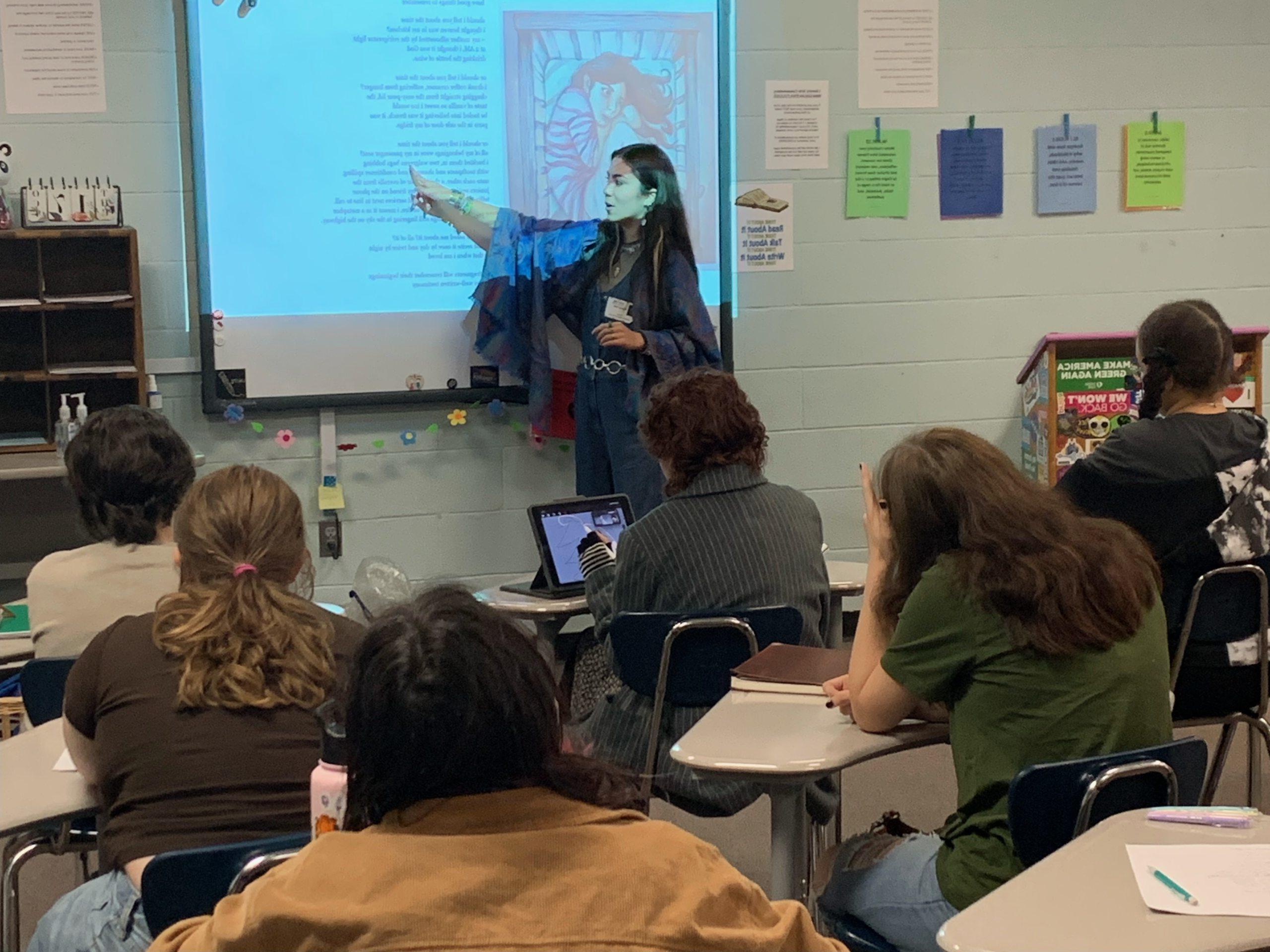 Mel Dalili in front of a high school class room teaching poetry to students.